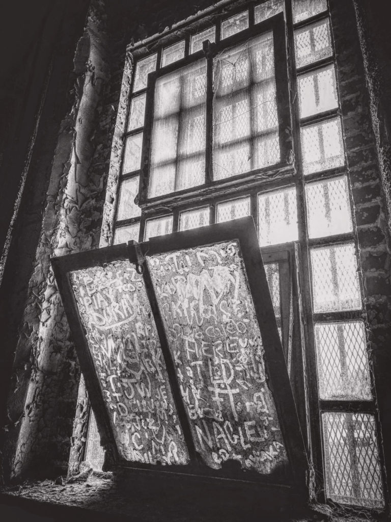Black and White photo of a window with messages written in the dirt by hand